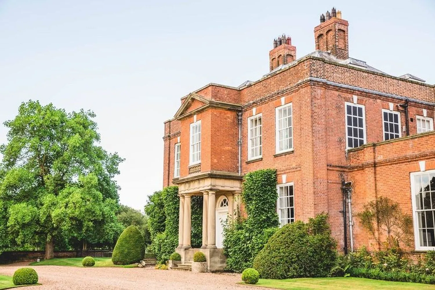 Iscoyd Park: a red-brick Georgian house with a pillared porch, clipped topiary and a gravel drive.