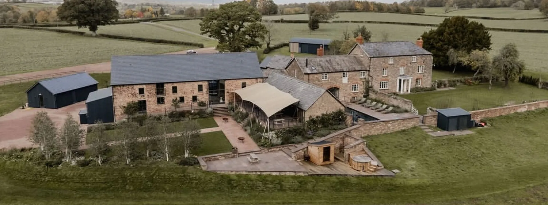 Llantilio House from the air: the barns, the farmhouse and the pool in open Welsh countryside.